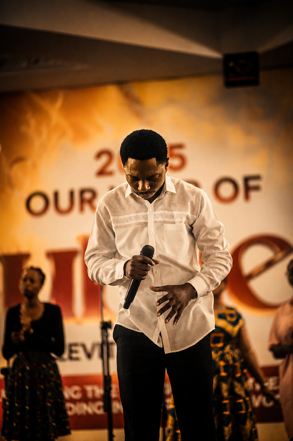 A worship leader with head bowed holding a microphone